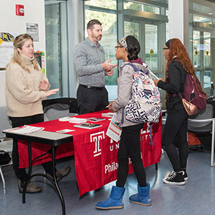 2 students talking to admission specialist from a visiting college at a dual admissions information table