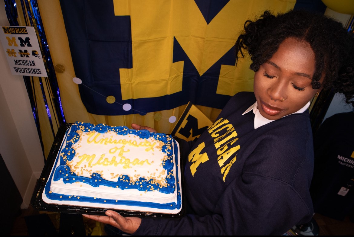 Antoinette Ellis holding a cake to celebrate her graduation, wearing University of Michigan Gear 
