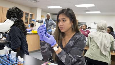 Student examines test tube while instructor speaks to the class in the background.