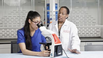 Instructor teaches a student how to use a microscope.