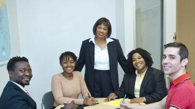 A group of five people in business attire, gathered around a table, smile for the camera.