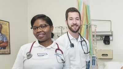 Two student nurses with stethoscopes in a classroom smile at the camera.