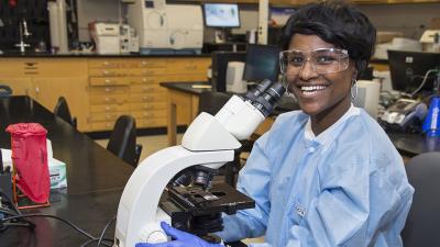 A smiling medical lab technologist seated at a microscope