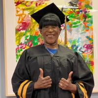 Tracey Downing in her graduation gown posing with two thumbs up