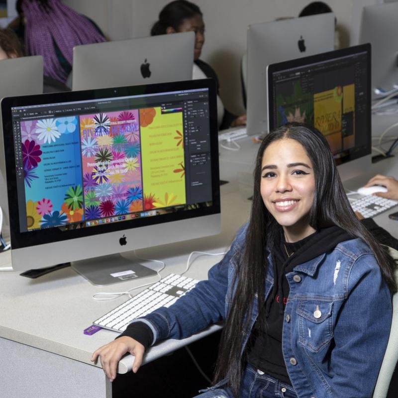Art student sitting in front of a monitor with her graphic designs on display