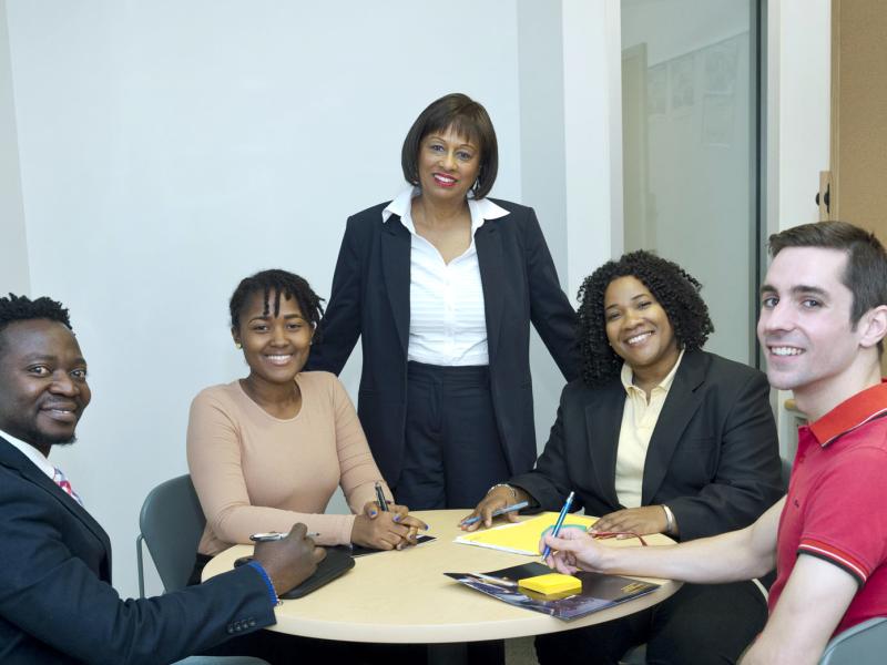 A group of five people in business attire, gathered around a table, smile for the camera.