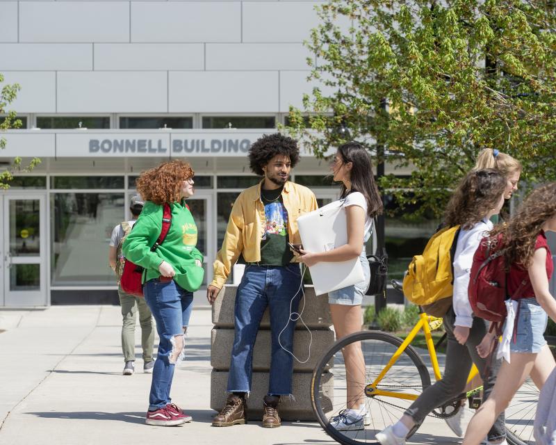 Three students talking and smiling in front of the Bonnell building