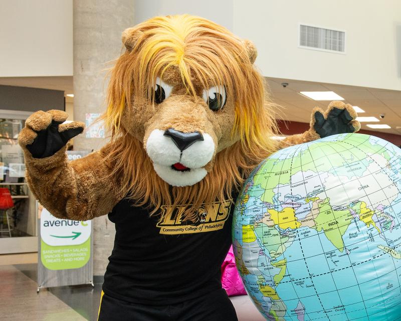 Roary the mascot playfully raises a paw to the camera while holding an inflatable globe.